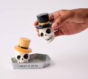 two skull shakers inside a coffin shaped holder. a hand is lifting one up. 