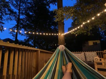 Person relaxing successful  a hammock connected  a platform  astatine  dusk, with drawstring  lights overhead creating a peaceful atmosphere
