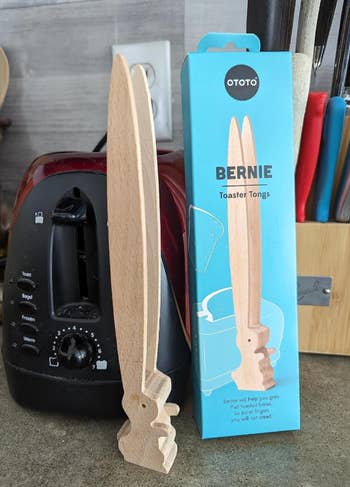 Wooden toaster tongs with a bunny design next to its packaging