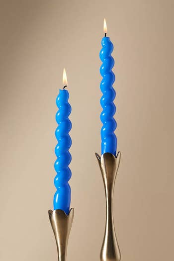 Two blue, spiral candles lit in elegant candle holders, possibly for a home decor shopping article
