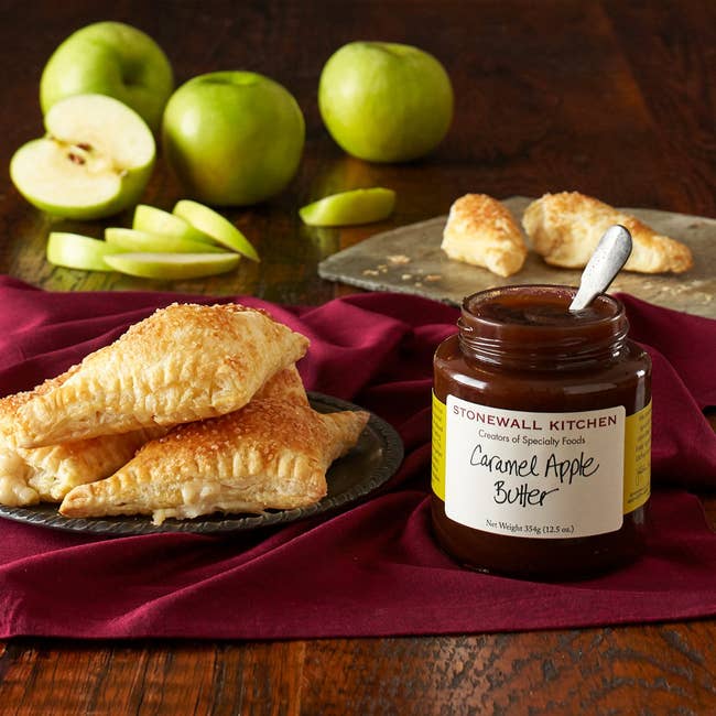 Stonewall Kitchen Caramel Apple Butter jar beside turnovers and sliced apples connected  a table