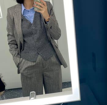 Person in a tailored grey suit with a blue shirt, taking a mirror selfie for a shopping-related article