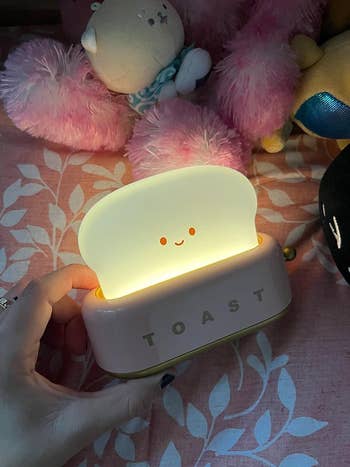 reviewer holding up the lit toast-shaped lamp in a dark room