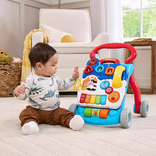 Baby plays with a colorful enactment   walker featuring buttons and toys successful  a cozy country   with an armchair and a handbasket  of blankets