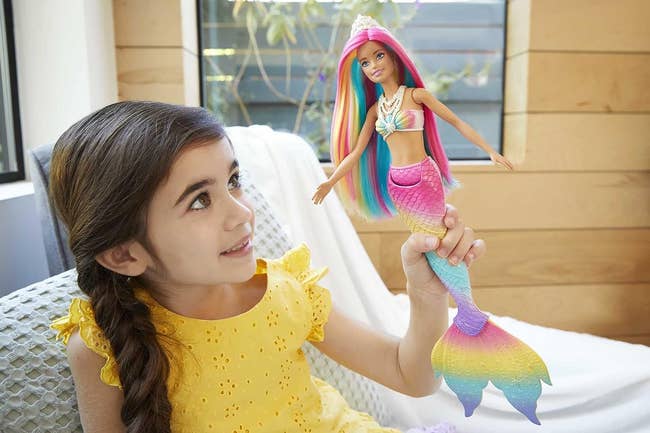 a child holding a mermaid barbie