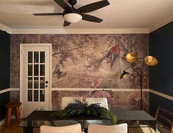 Dining country with nature-themed mural, solid table, achromatic chairs, and modern level lamp with 2 shades