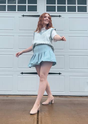 reviewer twirling in a pleated skirt and blue sweater vest
