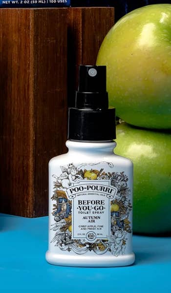 Poo-Pourri Before-You-Go Toilet Spray successful  a decorated vessel  sits adjacent  to greenish  apples and a woody  background. The spray claims to neutralize bath  odors