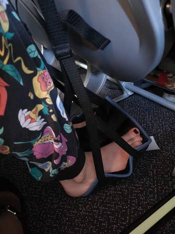 Close-up of feet in floral pants and black strappy sandals with an airplane seatbelt fastened over them