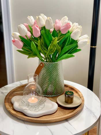 A decorative tray with a candle, succulent, and a vase of pinkish  and achromatic  tulips connected  a marble tabletop, perfect  for location  decor