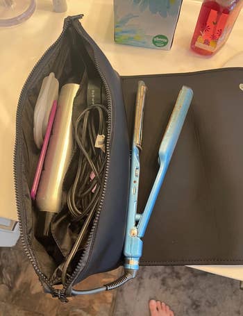 A black zippered compartment full of hair tools with a front flap resting on a counter with a straightener laying on it 