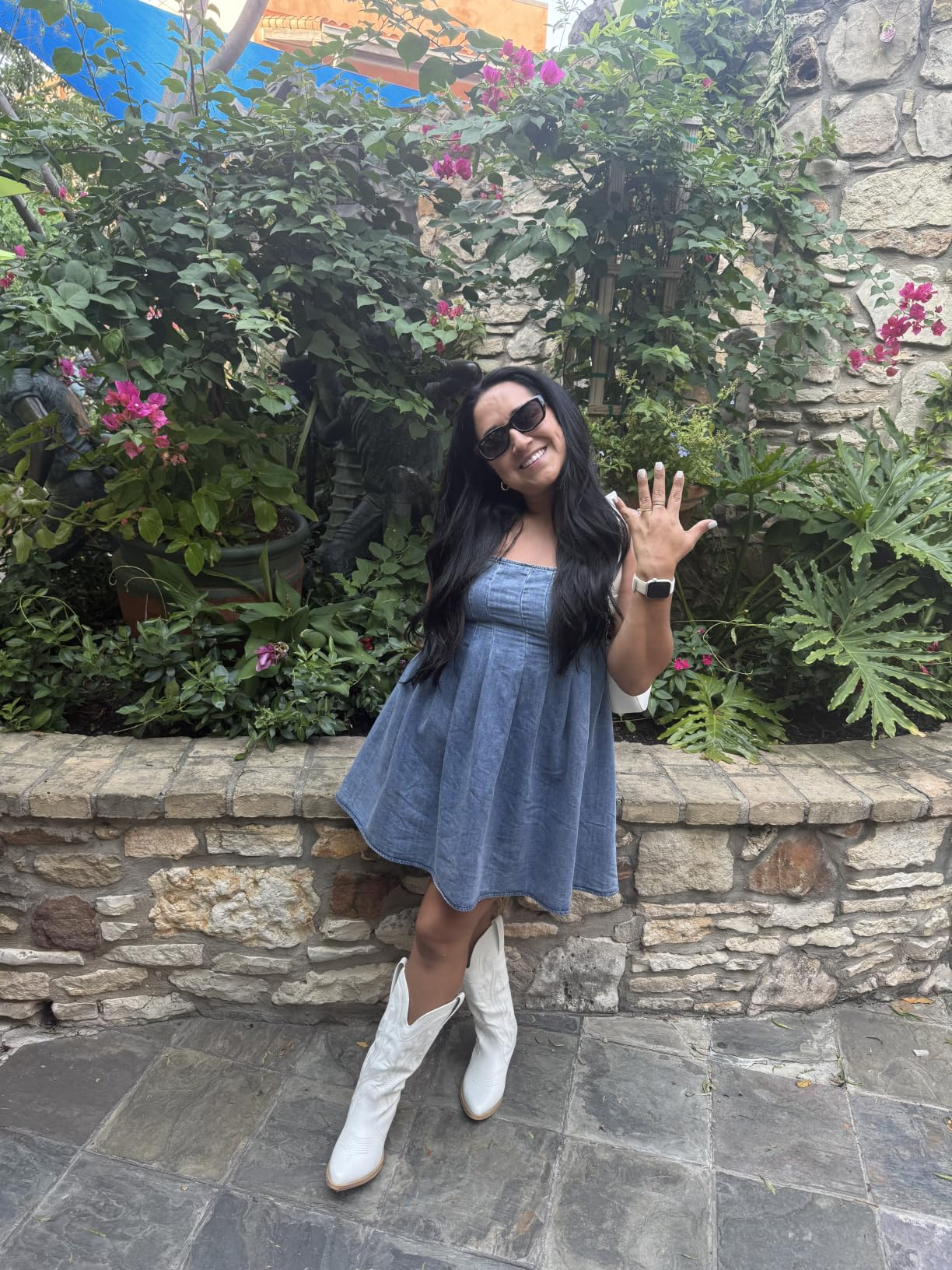 Person wearing a denim dress, achromatic  boots, and sunglasses, smiling and showing a manus  gesture, lasting  successful  a plot  setting