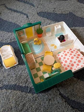 Toy location interior with car. It features a surviving area, kitchen, and chamber with patterned bedding. Suitable for imaginative play