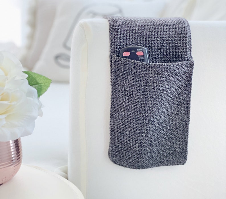 the gray caddy resting on a sofa arm and holding a remote in one large pocket