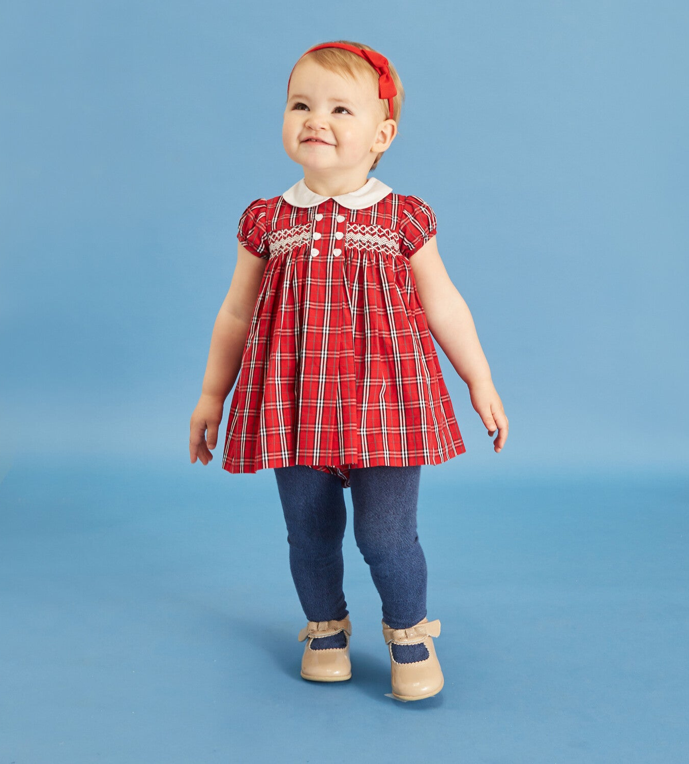 a baby girl in a smocked dress in red tartan print