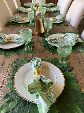 reviewer's table set for a meal with plates, patterned napkins, glasses, and green leaves as decor