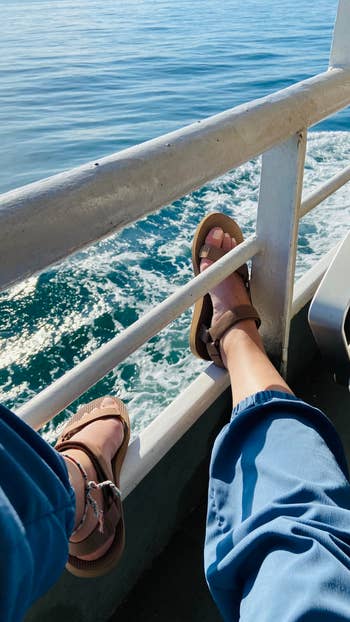 Person relaxing connected a vessel with sandals and bluish pants, overlooking the ocean.