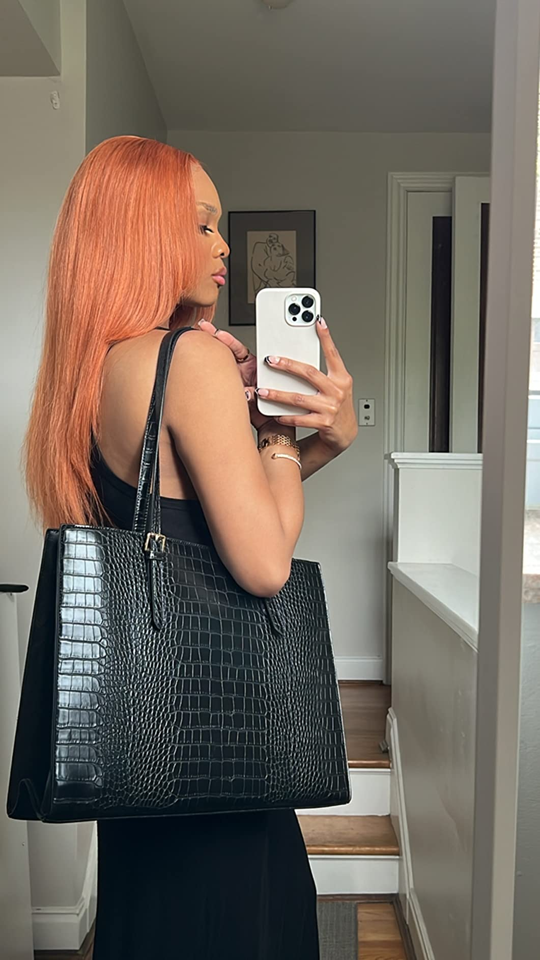 Person taking a mirror selfie, showcasing a large black crocodile-texture handbag and wearing a sleeveless black dress
