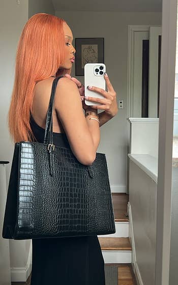 Person taking a mirror selfie, showcasing a large black crocodile-texture handbag and wearing a sleeveless black dress