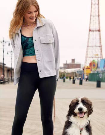 a model wearing a cropped gray fleece shacket with black leggings next to a dog