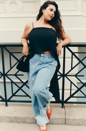 Person successful  a stylish, sleeveless apical  and wide-leg jeans, holding a purse, leaning against a railing. Fashionable look   suitable for casual outings