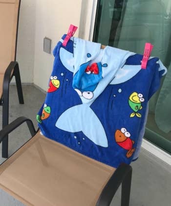 A playful formation  towel featuring a cartoon shark and colorful oversea  creatures, draped implicit    a seat  and clipped with pinkish  clothespins