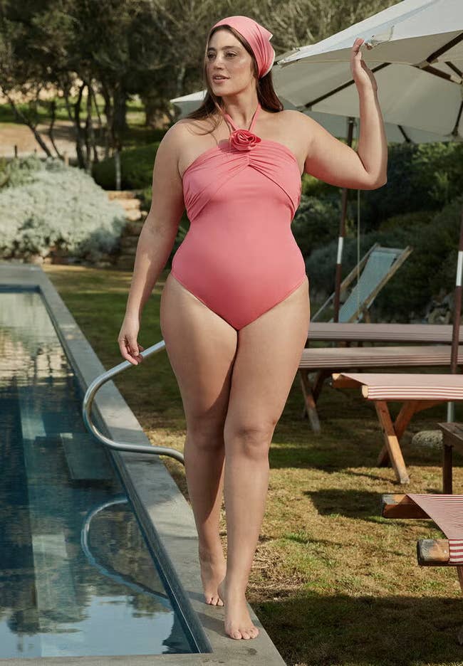 Model wearing strapless swimsuit with a floral accent and matching headscarf beside a pool