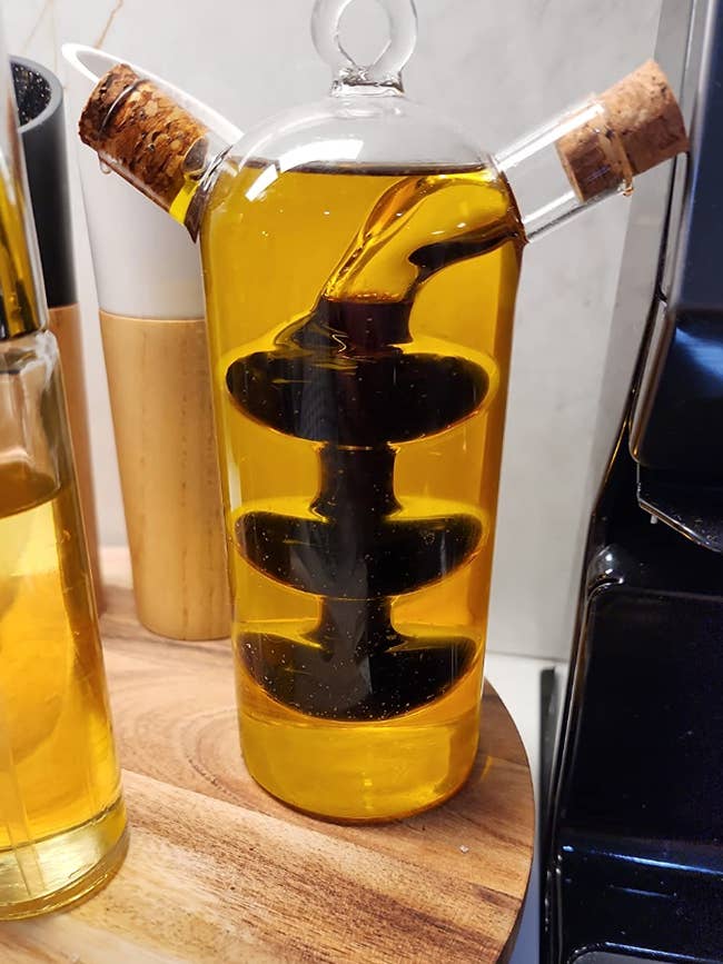 A dispenser filled with olive oil with a mini section that twists inside and holds vinegar, with two spouts coming out of either side of it 