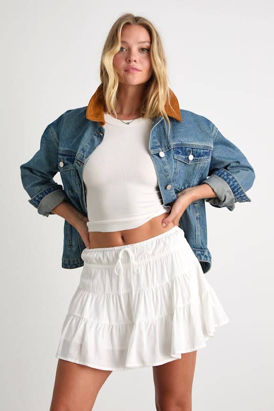Woman successful a denim overgarment implicit a achromatic harvest apical and tiered skirt, hands connected hips. Casual and trendy outfit for shopping