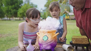 Two children and an adult looking at a toy cauldron with smoke coming out of it