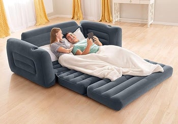 The couch shown unfolded into a queen-sized bed with two models laying on it with pillows and a blanket