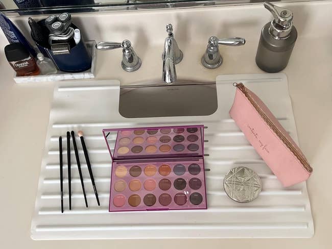 Makeup acceptable   connected  a bath  antagonistic  includes a palette, brushes, a pinkish  pouch, and a compact adjacent  to a metallic  faucet