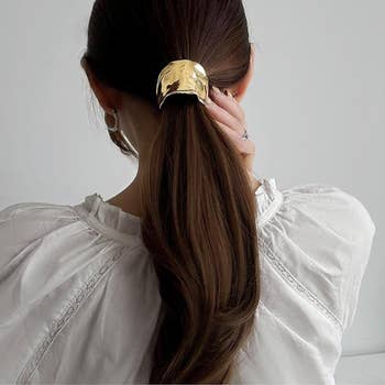 person with long hair tied in a low ponytail, secured with a large, shiny metal hair clip, wearing a white blouse with lace details