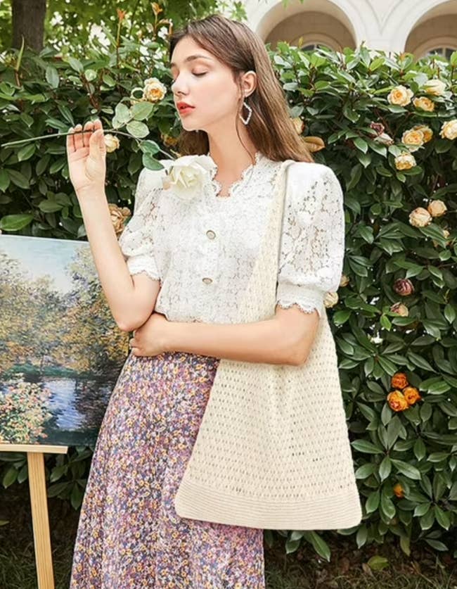 person successful  a lace blouse and floral skirt poses with a canvas container  adjacent   a coating  and garden