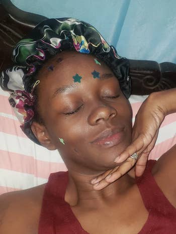 Person lying down   with eyes closed, wearing a satin bonnet and star-shaped stickers connected  face