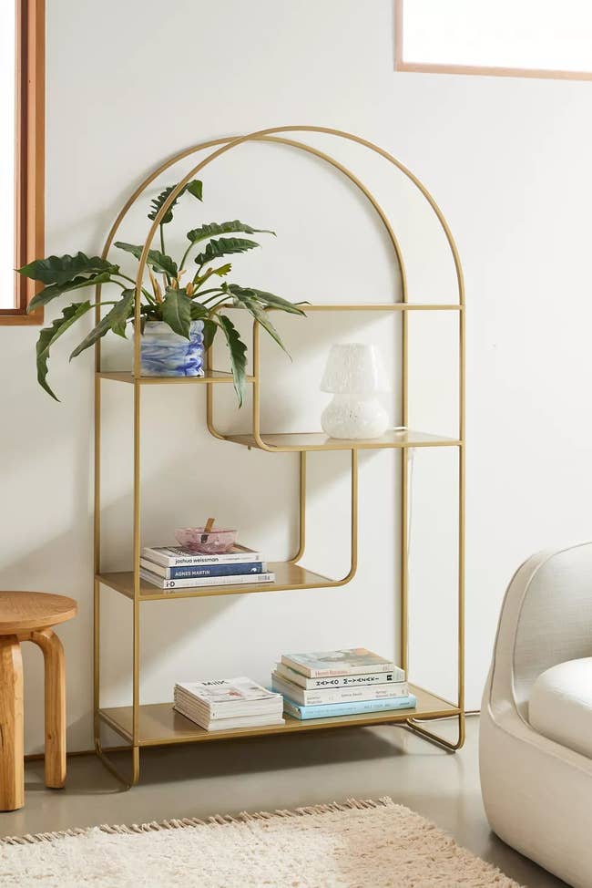Metal arched bookshelf with five shelves, holding books, a plant, and decor items
