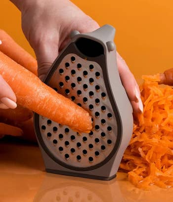 Hand grating a carrot with a handheld grater over a pile of shredded carrots
