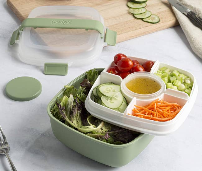A bento-style lunch box with compartments for salad, vegetables, and dressing