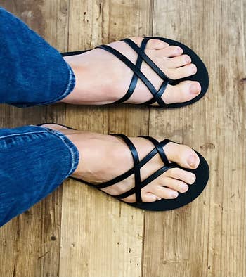 Person wearing strappy flat sandals and blue jeans, viewed from above. Perfect for a casual summer outfit
