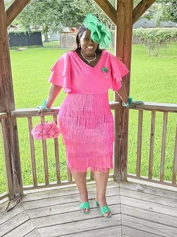Person successful a pinkish fringed formal and greenish floral headpiece stands smiling nether a gazebo, accessorized with pinkish purse and greenish mules