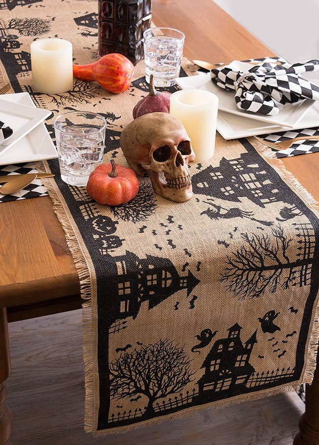 burlap runner with halloween theme pattern in black. placed on decorated table. 