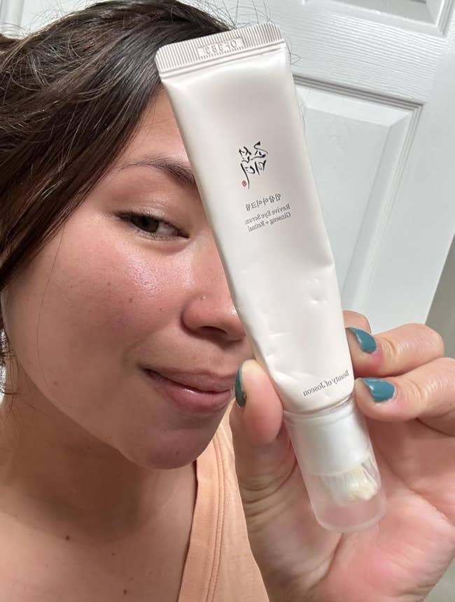 A idiosyncratic holding a conduit of facial cleanser adjacent to their face, showing creaseless skin
