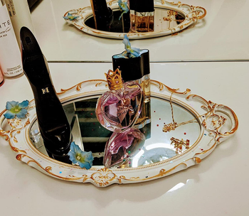 perfume and other small items on a white and gold mirror being used as a tray