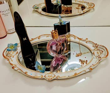perfume and other small items on a white and gold mirror being used as a tray