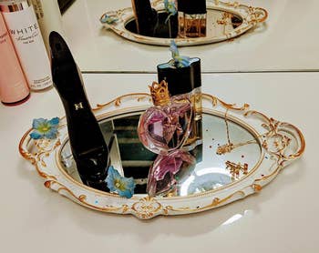 perfume and other small items on a white and gold mirror being used as a tray