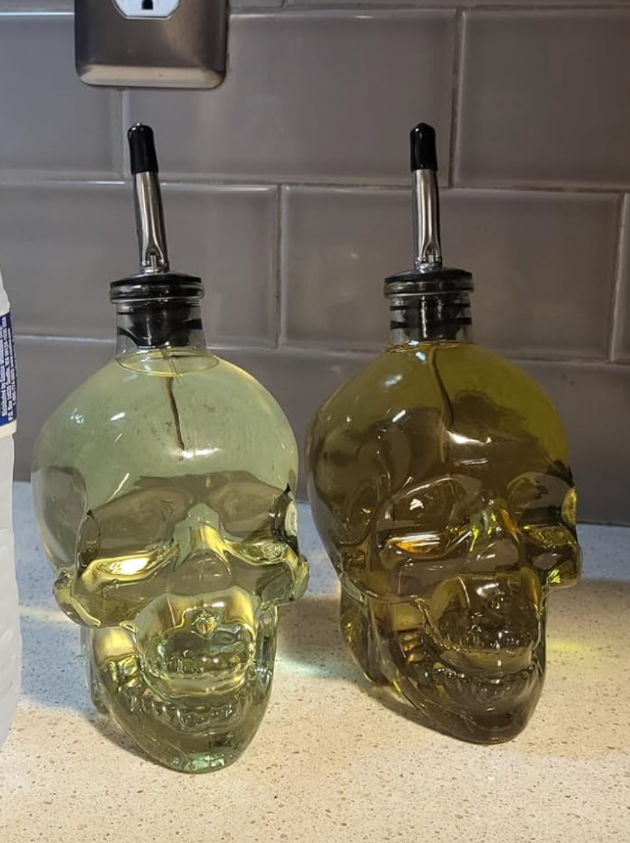 Two clear skull-shaped dispensers full of olive oil 