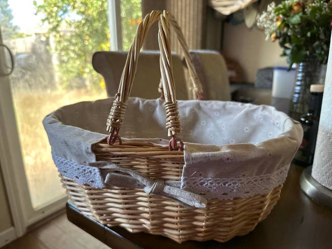 Woven wicker handbasket with cloth lining and bow detail, placed connected a array adjacent a model with a presumption of trees outside
