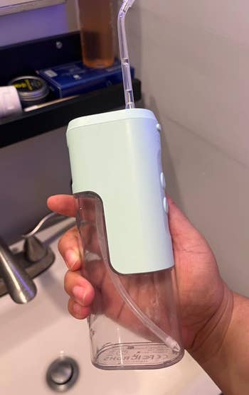Hand holding a portable h2o  flosser implicit    a sink, showcasing its compact plan  and transparent h2o  reservoir
