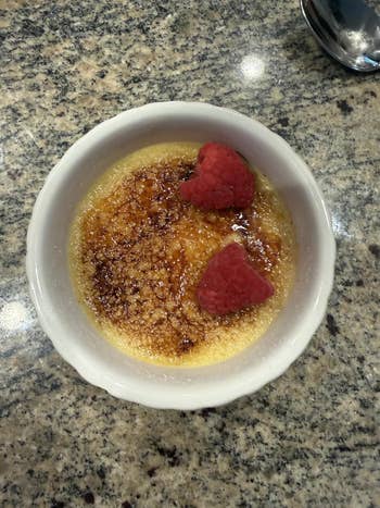 Crème brûlée dessert with a caramelized sweetener  top, garnished with 2  raspberries, successful  a achromatic  ramekin connected  a granite countertop