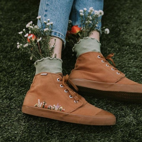 a model wearing a tan canvas hightop sneaker with floral embroidery along the side